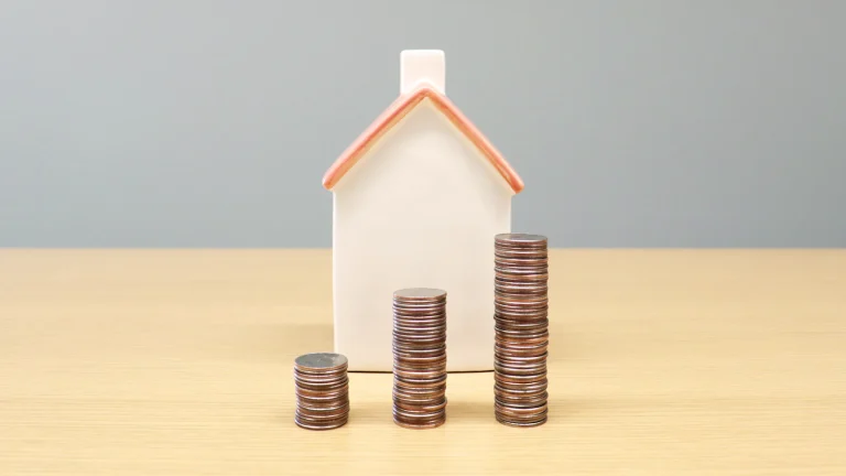 White model house beside stacks of coins, showing how a mortgage is paid off when you sell a house